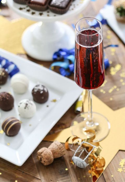 Kir Royale Cassis black currant liquer champagne cocktail with assorted chocolate red velvet and peanut butter cake truffles on a white plate and a cork